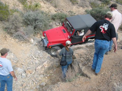 1996 Ford Bronco - A red Jeep Wrangler maneuvers through a challenging off-road course with onlookers observing the action.