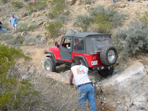 1996 Ford Bronco - A red Jeep Wrangler navigates a rocky trail, with a person assisting from the side.