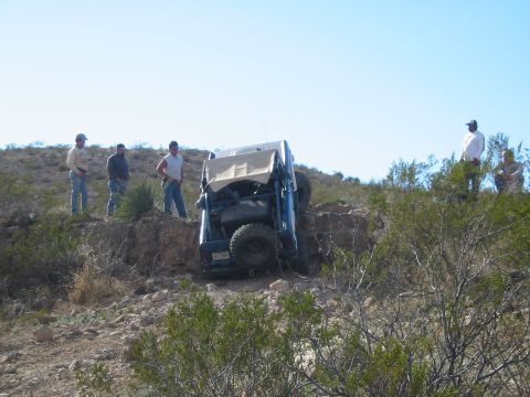1996 Ford Bronco - A group of people observe an off-road vehicle that has tipped onto its side on a rocky hill.