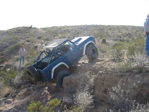 1996 Ford Bronco - A modified blue SUV navigates a steep, rocky incline in a desert landscape.