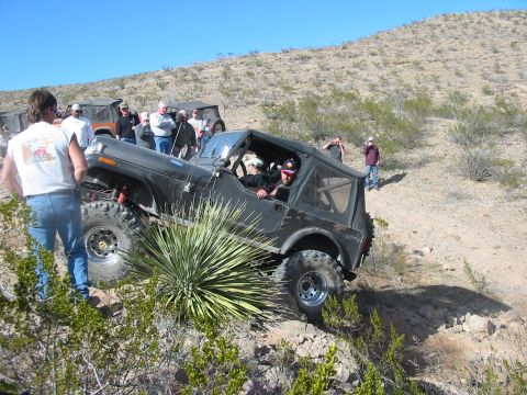 1996 Ford Bronco - A black Jeep CJ-7 is shown off-roading on a sunny day, with several people watching the action.