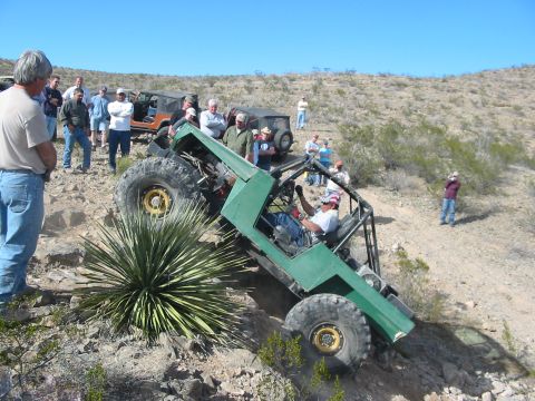 1996 Ford Bronco - A group watches as a custom off-road buggy navigates a steep, rocky incline under a clear blue sky.