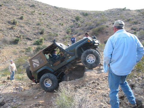 1996 Ford Bronco - A Jeep Wrangler is shown off-roading on a steep, rocky incline with onlookers present.