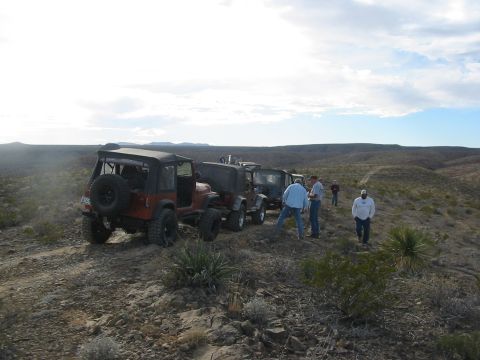 1996 Ford Bronco - A group of Jeeps are parked on a dusty trail in a desert landscape under a cloudy sky.