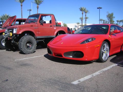 1987 Suzuki Samurai - A red Ferrari and a modified red Suzuki Samurai are parked side-by-side in a lot.