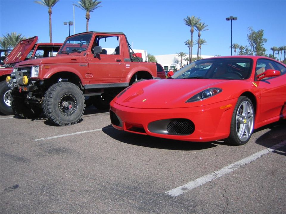 Red Ferrari parked next to a lifted red Suzuki Samurai with large tires