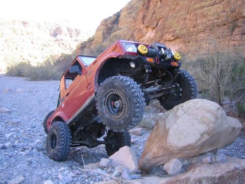 1987 Suzuki Samurai - Modified 1987 Suzuki Samurai navigating a rocky obstacle in a desert environment.