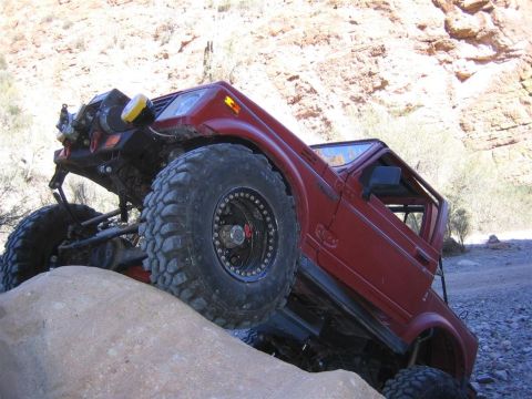 1987 Suzuki Samurai - A red 1987 Suzuki Samurai navigates a rocky terrain with its tires angled on a large boulder.