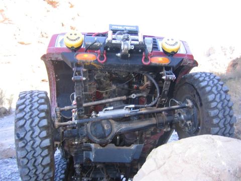 1987 Suzuki Samurai - This heavily modified off-road vehicle shows its robust front axle and suspension system, equipped with a winch and auxiliary lights.