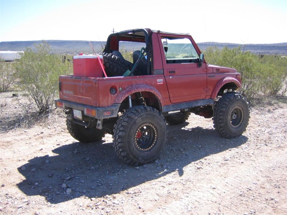 Red 1987 Suzuki Samurai with oversized tires and a cooler in the bed