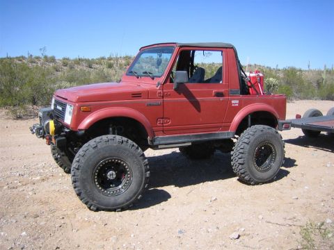 1987 Suzuki Samurai - A red 1987 Suzuki Samurai is parked on a dirt road in a desert landscape, hitched to a trailer.