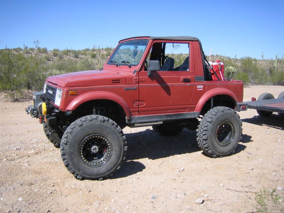 Red 1987 Suzuki Samurai with large off-road tires and a trailer hitch