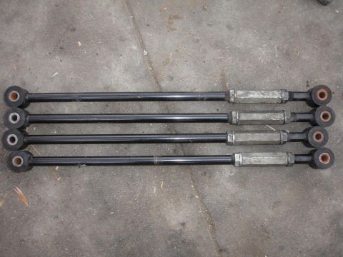 1992 Ford Taurus - Four black suspension control arms are laid out on a gray concrete surface, showing their adjustable metal sleeves and rubber bushings.