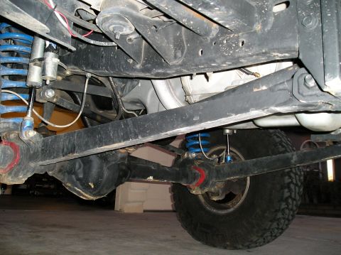 1993 Ford Bronco - The undercarriage of a vehicle shows a modified suspension system with prominent blue coilover shocks and a off-road tire.