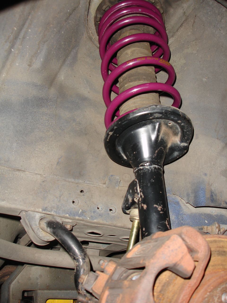 Close-up of a car's front suspension with a purple coilover shock and brake caliper