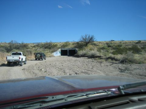 1996 Ford Bronco - Two vehicles travel on a dusty road towards a tunnel entrance in a dry, arid landscape under a clear blue sky.
