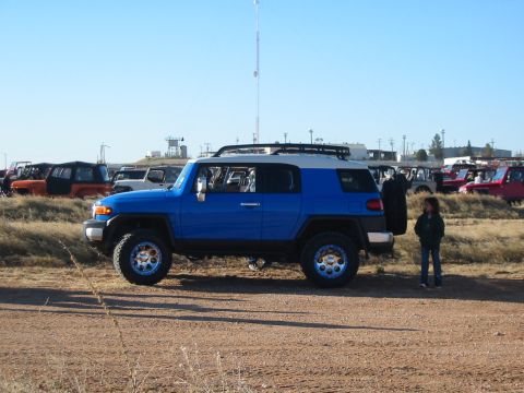 1996 Ford Bronco - A blue SUV with a white roof is parked in a lot with other vehicles under a clear blue sky.