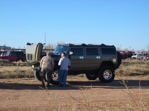 1996 Ford Bronco - Two individuals examine the engine of a brown Hummer H2, which has its hood raised, under a clear blue sky.