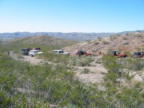 1996 Ford Bronco - A convoy of SUVs and Jeeps navigates a dusty trail in a dry, hilly terrain under a clear blue sky.