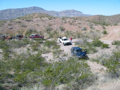1996 Ford Bronco - Several off-road vehicles are parked on a dirt path in a dry, hilly landscape under a clear blue sky.