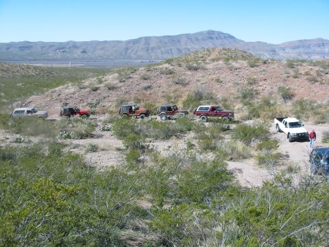 1996 Ford Bronco - A convoy of SUVs and trucks navigates a dusty, arid landscape under a clear blue sky.