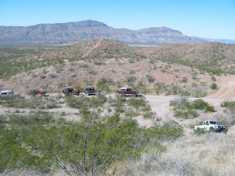 1996 Ford Bronco - A convoy of off-road vehicles navigates a dusty trail in a vast, arid landscape under a clear blue sky.