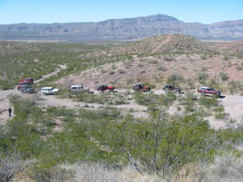 1996 Ford Bronco - A group of off-road vehicles are stopped on a dusty trail in a dry, mountainous region.