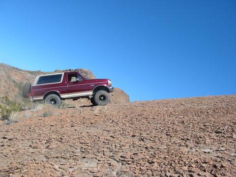 1996 Ford Bronco - A maroon Ford Bronco navigates a rocky desert terrain on a clear day.