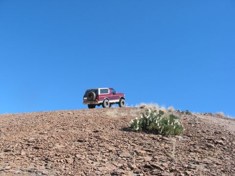 1996 Ford Bronco - A red SUV, likely a 1992 Ford Bronco, is parked on a rocky incline with a spare tire mounted on the rear door.