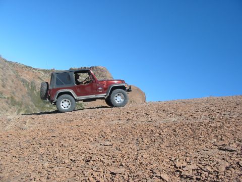 1996 Ford Bronco - A red Jeep Wrangler navigates a rocky incline on a clear day.