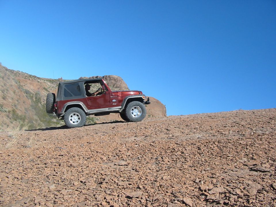 Red Jeep Wrangler driving on a rocky hill under a clear blue sky