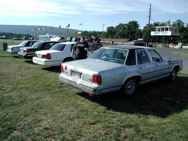 White Ford LTD Crown Victoria sedan rear view, parked on grass with other Ford sedans at an outdoor event