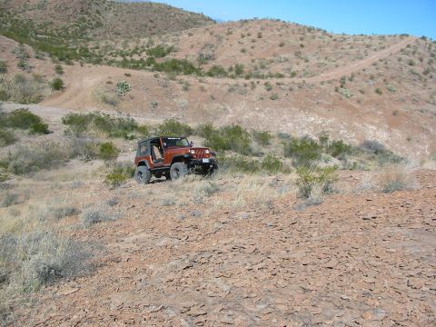 1996 Ford Bronco - An orange Jeep Wrangler is parked on a rocky hillside under a clear blue sky.