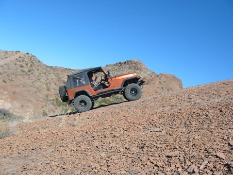 1996 Ford Bronco - Jeep Wrangler navigates a challenging off-road trail in a desert landscape.