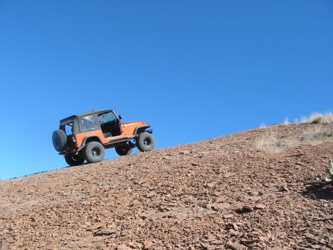 1996 Ford Bronco - An orange Jeep Wrangler ascends a steep, rocky incline on a clear day.