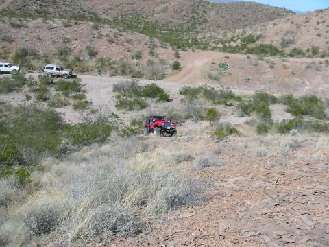 1996 Ford Bronco - Multiple off-road vehicles traverse a dusty, arid terrain under a clear sky.