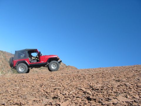 1996 Ford Bronco - Red Jeep Wrangler navigates a steep, rocky incline on a clear day.