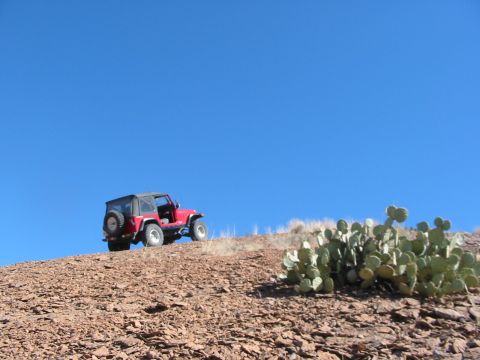 1996 Ford Bronco - A red Jeep Wrangler sits on a desolate, rocky hillside with a bright blue sky overhead.