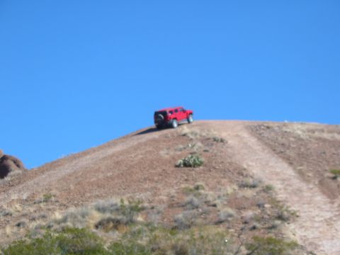 1996 Ford Bronco - A red SUV is parked on a dirt path on a hill with a clear blue sky above.