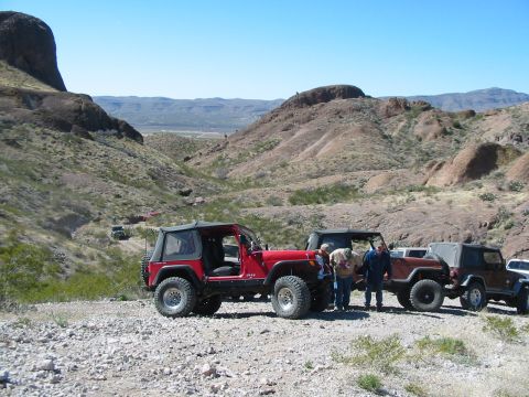 1996 Ford Bronco - A group of Jeeps are parked on a dirt road in a mountainous desert area under a clear blue sky.