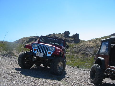 1996 Ford Bronco - Two Jeeps are parked on a dusty, rocky trail with hills in the background under a clear blue sky.