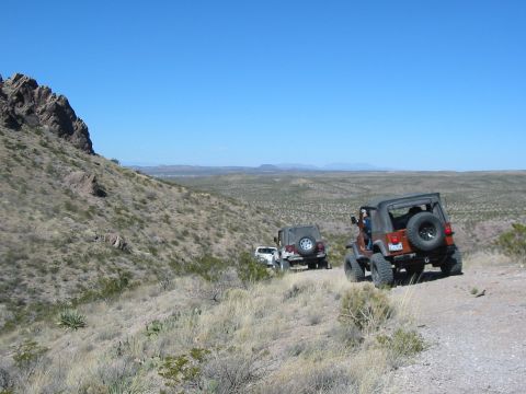 1996 Ford Bronco - Several Jeeps navigate a dusty trail through a desert landscape under a clear blue sky.