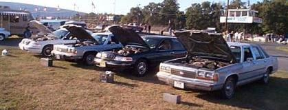 1989 Ford Crown Victoria LTD - Several sedans, likely from the 1980s, are parked with their hoods open at an outdoor event.