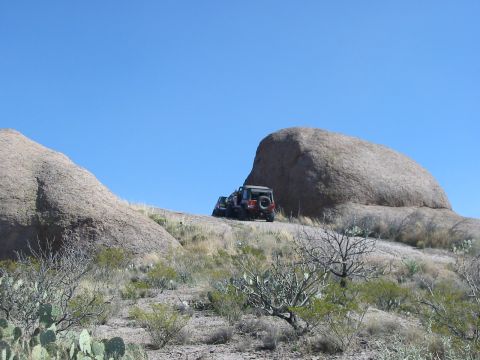 1996 Ford Bronco - Two off-road vehicles are parked on a dirt path on a rocky hill with sparse vegetation.
