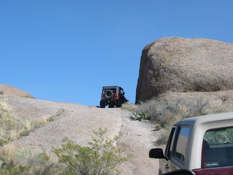1996 Ford Bronco - Two off-road vehicles navigate a rocky, desert landscape under a clear blue sky.