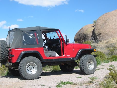 1996 Ford Bronco - A red Jeep Wrangler with a soft top is parked on a dirt road with large rocks in the background.