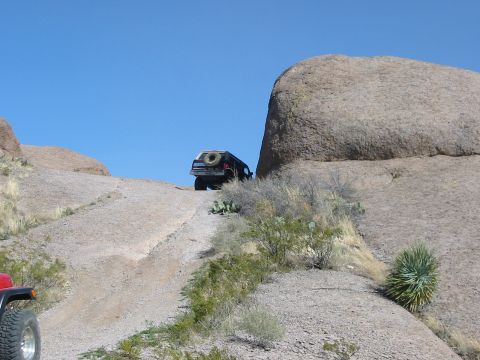 1996 Ford Bronco - An off-road vehicle navigates a steep, rocky incline under a clear blue sky.
