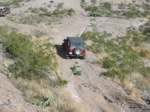 1996 Ford Bronco - Two off-road vehicles navigate a steep, dusty trail through a dry, arid environment.