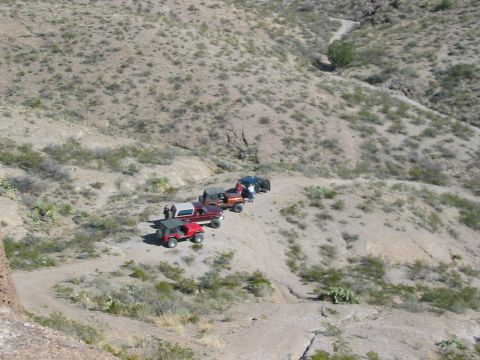 1996 Ford Bronco - Several off-road vehicles navigate a winding dirt path through a dry, arid landscape.