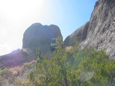 1996 Ford Bronco - An SUV navigates a challenging off-road trail with steep, rocky terrain and sparse vegetation under a clear blue sky.
